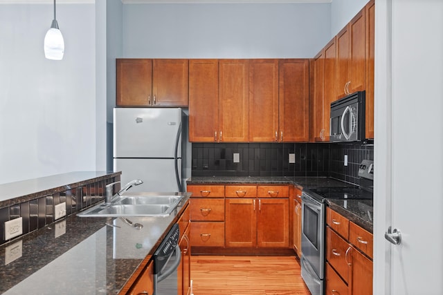 kitchen featuring hanging light fixtures, sink, dark stone counters, appliances with stainless steel finishes, and light wood-type flooring