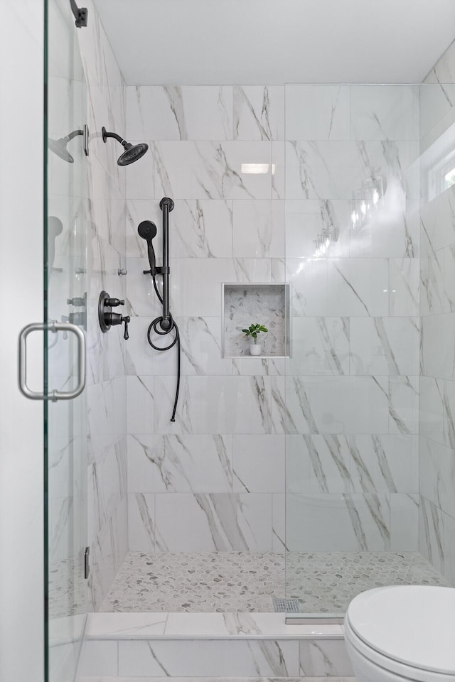 bathroom featuring a shower with door and toilet