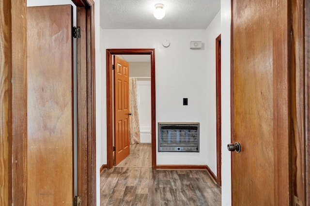 hall featuring heating unit, a textured ceiling, and hardwood / wood-style flooring