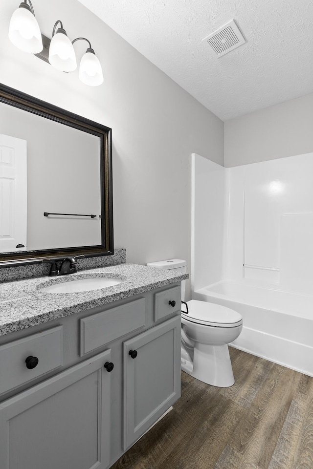 full bathroom featuring a textured ceiling, hardwood / wood-style flooring, bathing tub / shower combination, vanity, and toilet