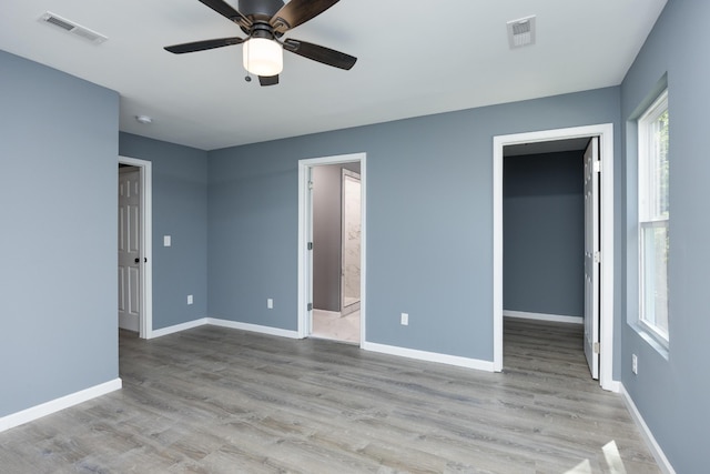 unfurnished bedroom with light wood-type flooring, ensuite bath, ceiling fan, and a walk in closet