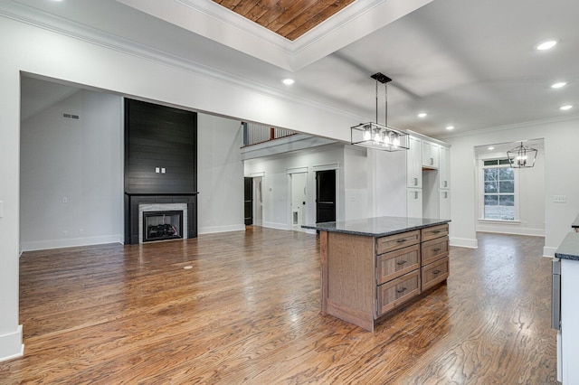 kitchen with a large fireplace, dark stone countertops, pendant lighting, white cabinets, and hardwood / wood-style flooring