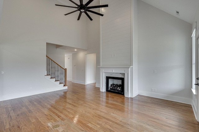 unfurnished living room featuring a premium fireplace, ceiling fan, light hardwood / wood-style flooring, and high vaulted ceiling