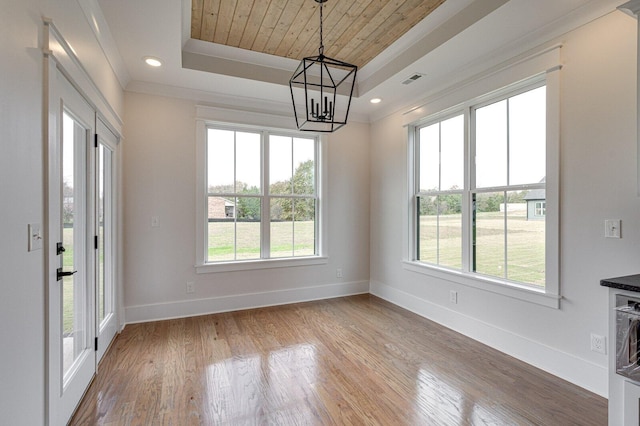 unfurnished dining area featuring wood-type flooring, a notable chandelier, a healthy amount of sunlight, and a raised ceiling