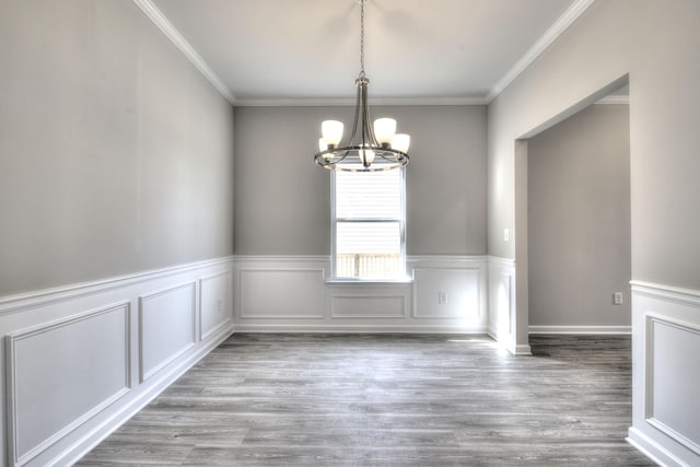 unfurnished dining area featuring an inviting chandelier, crown molding, and light hardwood / wood-style floors