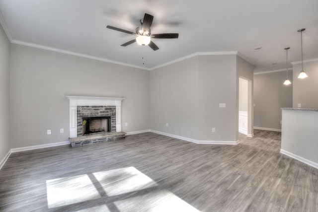 unfurnished living room with ceiling fan, a stone fireplace, ornamental molding, and wood-type flooring