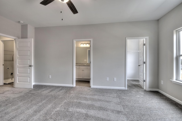 unfurnished bedroom with a closet, light colored carpet, ensuite bathroom, a spacious closet, and ceiling fan