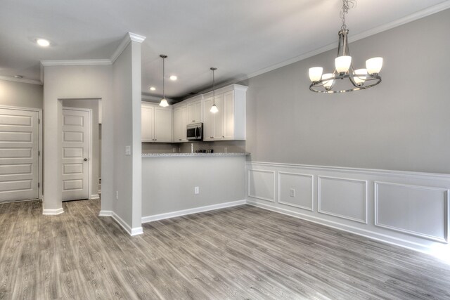 kitchen featuring ornamental molding, kitchen peninsula, decorative light fixtures, light hardwood / wood-style flooring, and white cabinetry