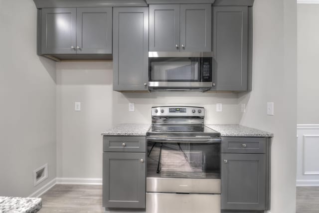 kitchen with appliances with stainless steel finishes, light wood-type flooring, gray cabinets, and light stone counters