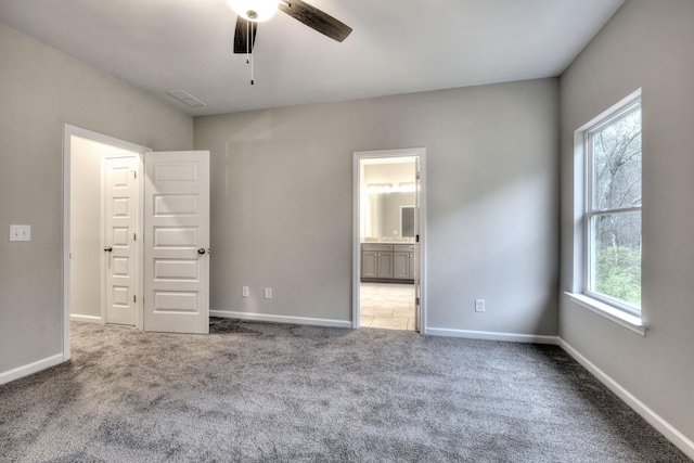 unfurnished bedroom with multiple windows, carpet flooring, ceiling fan, and ensuite bathroom