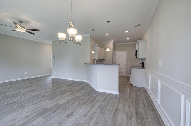 kitchen with pendant lighting, sink, ceiling fan with notable chandelier, white cabinets, and ornamental molding