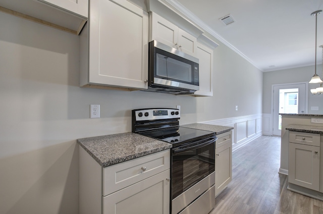 kitchen featuring appliances with stainless steel finishes, hanging light fixtures, dark stone countertops, light wood-type flooring, and crown molding