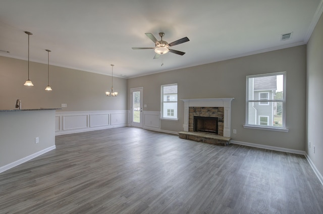 unfurnished living room featuring ceiling fan with notable chandelier, ornamental molding, dark wood-type flooring, and a stone fireplace