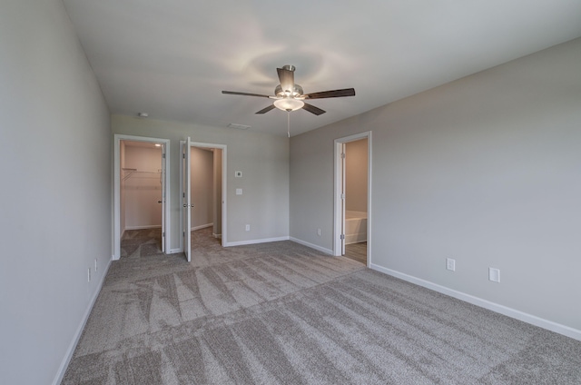 unfurnished bedroom featuring a closet, light colored carpet, a walk in closet, ensuite bathroom, and ceiling fan