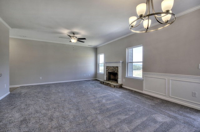 unfurnished living room with ceiling fan with notable chandelier, a fireplace, crown molding, and dark colored carpet