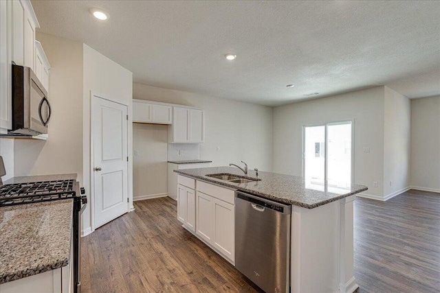 kitchen featuring appliances with stainless steel finishes, white cabinetry, stone countertops, a kitchen island with sink, and sink