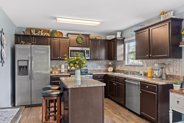 kitchen with a kitchen island, wood-type flooring, dark brown cabinets, backsplash, and appliances with stainless steel finishes