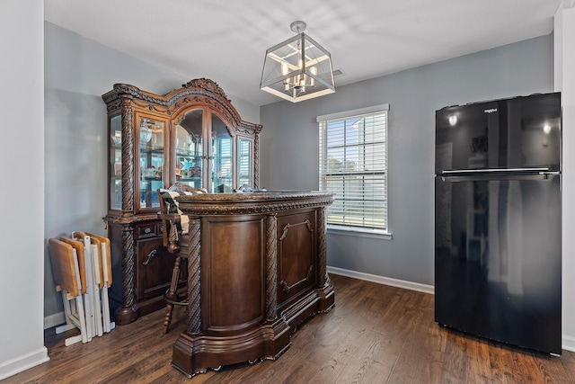 bar featuring an inviting chandelier, black refrigerator, hanging light fixtures, and dark hardwood / wood-style flooring