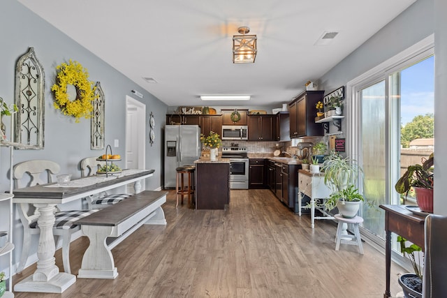 kitchen with dark brown cabinetry, light hardwood / wood-style flooring, appliances with stainless steel finishes, a center island, and decorative backsplash