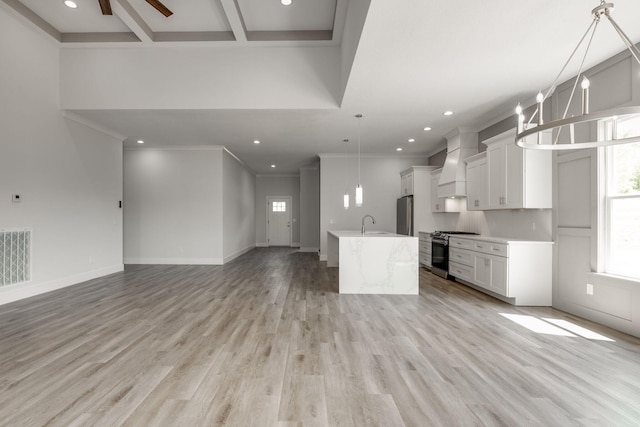 kitchen featuring pendant lighting, light hardwood / wood-style floors, stainless steel gas range oven, custom exhaust hood, and ceiling fan