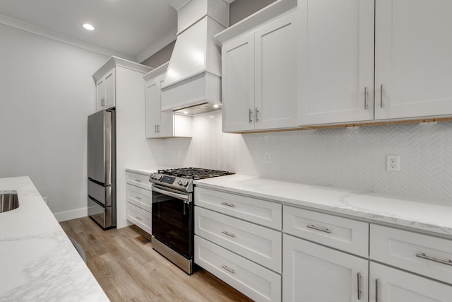 kitchen with appliances with stainless steel finishes, light hardwood / wood-style floors, white cabinets, light stone countertops, and premium range hood