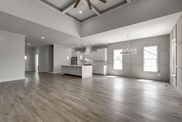 unfurnished living room with beamed ceiling, ceiling fan with notable chandelier, coffered ceiling, light hardwood / wood-style flooring, and ornamental molding