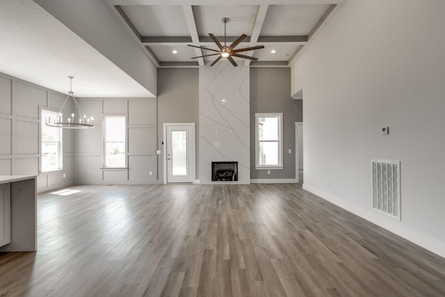 unfurnished living room featuring ceiling fan with notable chandelier, beam ceiling, a high end fireplace, and a healthy amount of sunlight