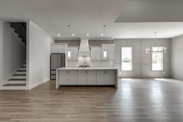 kitchen featuring light hardwood / wood-style flooring, white cabinetry, a kitchen island with sink, and custom exhaust hood