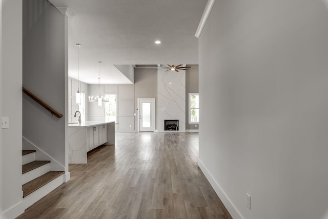 hallway with a textured ceiling, light hardwood / wood-style flooring, ornamental molding, sink, and a chandelier