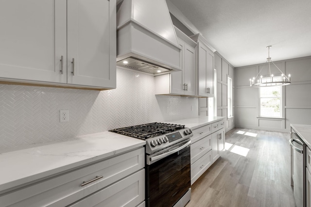 kitchen featuring light wood-type flooring, white cabinets, an inviting chandelier, stainless steel appliances, and premium range hood