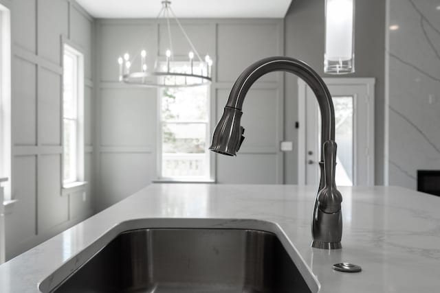 details with light stone counters, white cabinetry, a chandelier, and sink