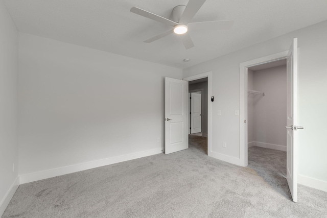 unfurnished bedroom featuring ceiling fan, a closet, light carpet, and a walk in closet