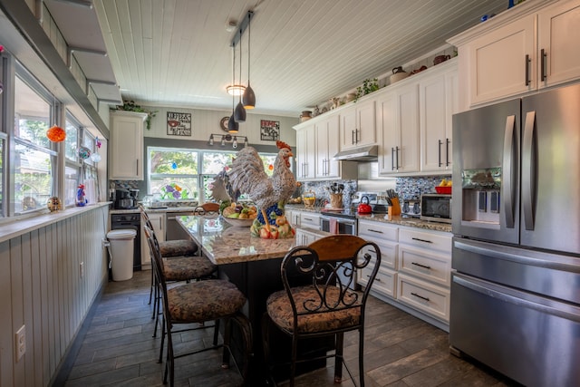 kitchen with a kitchen island, appliances with stainless steel finishes, light stone countertops, dark hardwood / wood-style floors, and pendant lighting