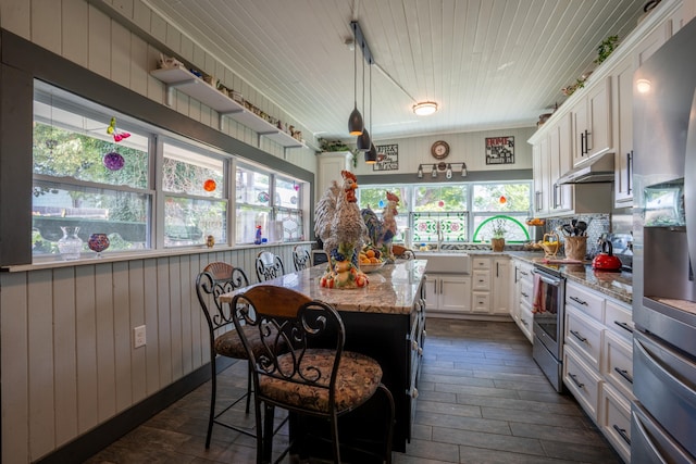 kitchen featuring a wealth of natural light, a center island, white cabinetry, and light stone counters