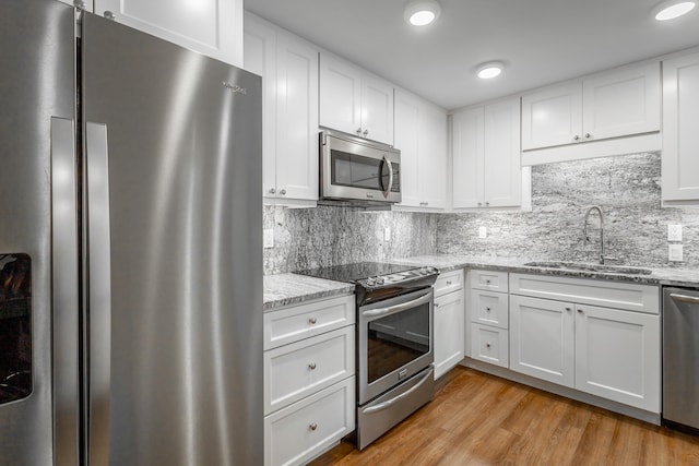 kitchen featuring white cabinets, sink, light hardwood / wood-style flooring, stainless steel appliances, and decorative backsplash