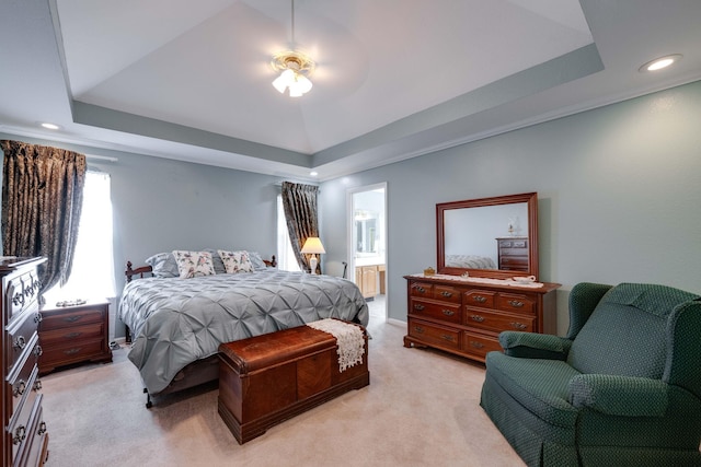 bedroom featuring light carpet, connected bathroom, a tray ceiling, and ceiling fan