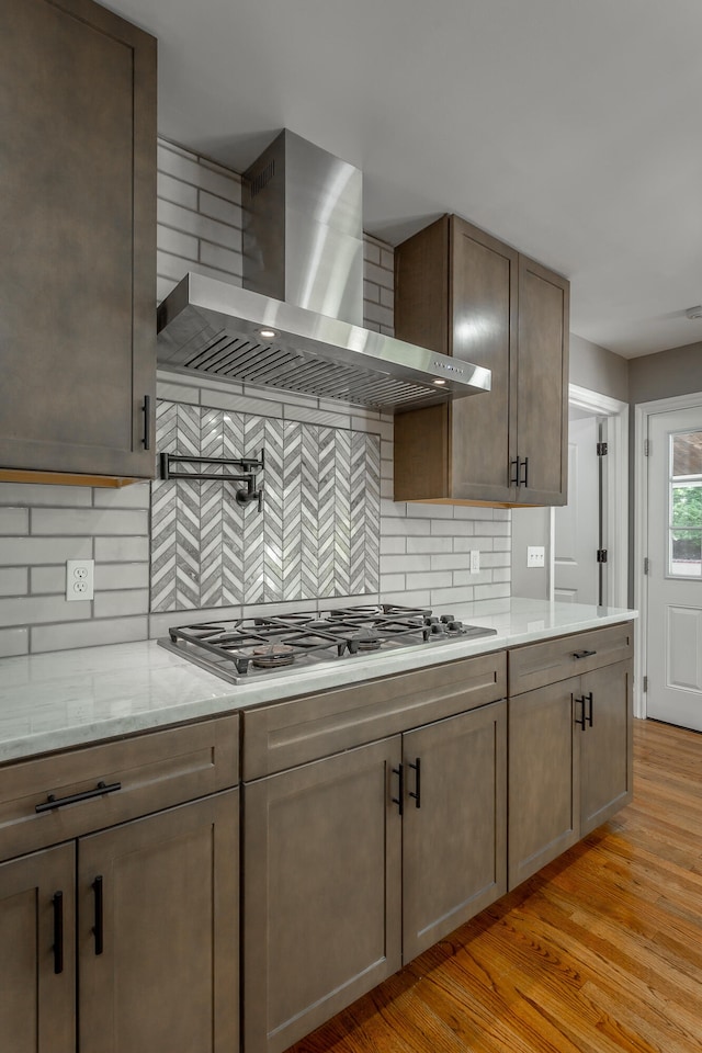 kitchen with tasteful backsplash, stainless steel gas stovetop, light hardwood / wood-style flooring, wall chimney exhaust hood, and light stone counters