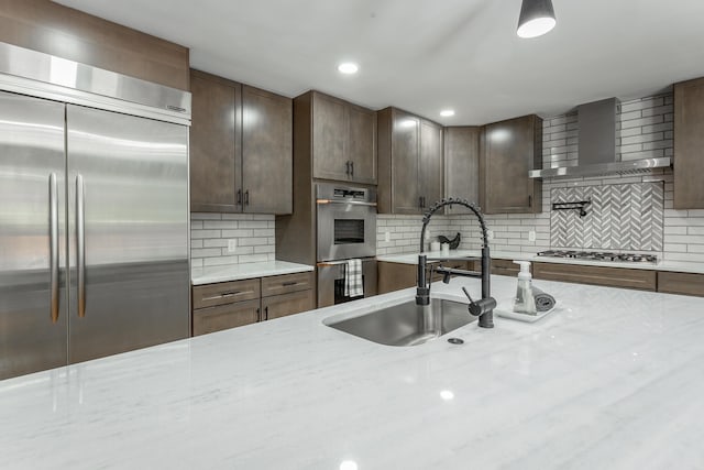 kitchen featuring wall chimney range hood, light stone countertops, appliances with stainless steel finishes, and decorative backsplash