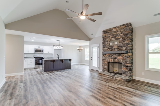 unfurnished living room featuring high vaulted ceiling, sink, light hardwood / wood-style flooring, ceiling fan, and a fireplace