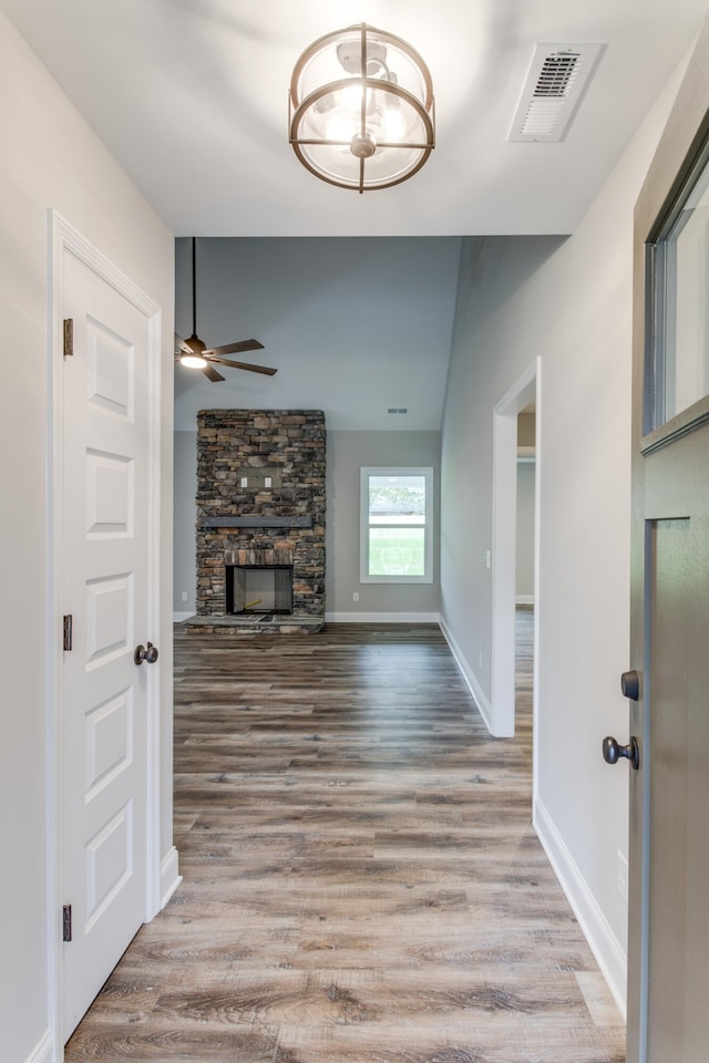 unfurnished living room featuring ceiling fan, a stone fireplace, and light wood-type flooring