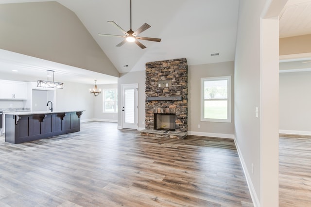 unfurnished living room with ceiling fan, sink, high vaulted ceiling, a fireplace, and hardwood / wood-style floors