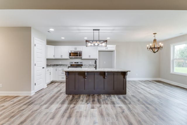 kitchen featuring light wood-type flooring, stainless steel appliances, a kitchen island with sink, white cabinets, and hanging light fixtures