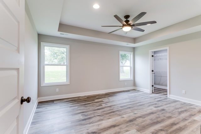 unfurnished room featuring a raised ceiling, ceiling fan, and light wood-type flooring