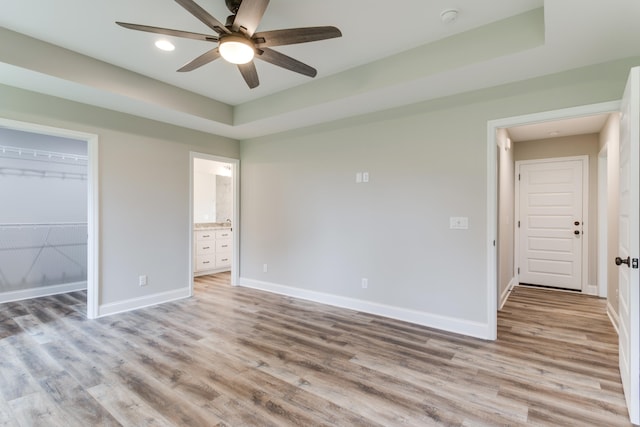 unfurnished bedroom featuring ensuite bath, ceiling fan, a spacious closet, a closet, and light wood-type flooring