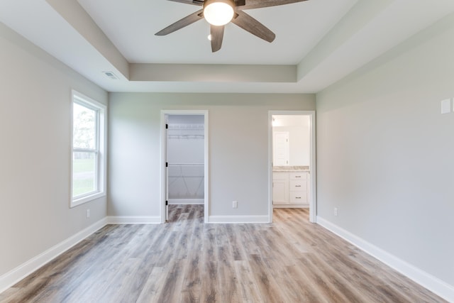 unfurnished bedroom with ceiling fan, light hardwood / wood-style floors, a walk in closet, and a tray ceiling