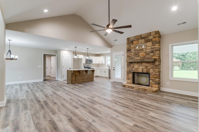 unfurnished living room featuring ceiling fan with notable chandelier, light hardwood / wood-style floors, a fireplace, and high vaulted ceiling