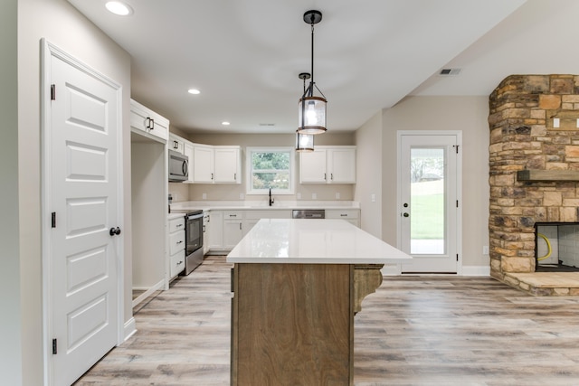 kitchen with appliances with stainless steel finishes, sink, light hardwood / wood-style flooring, white cabinets, and a kitchen island