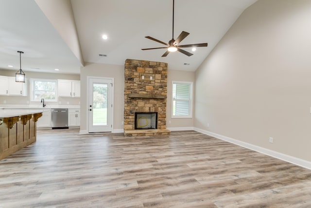 unfurnished living room featuring ceiling fan, sink, high vaulted ceiling, light hardwood / wood-style floors, and a stone fireplace