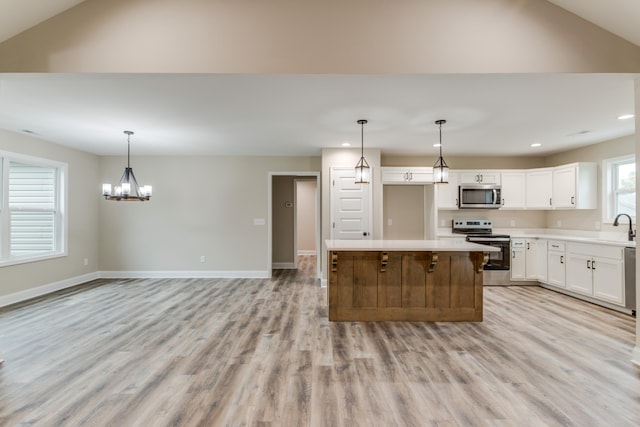 kitchen with pendant lighting, light wood-type flooring, a kitchen island, white cabinetry, and stainless steel appliances