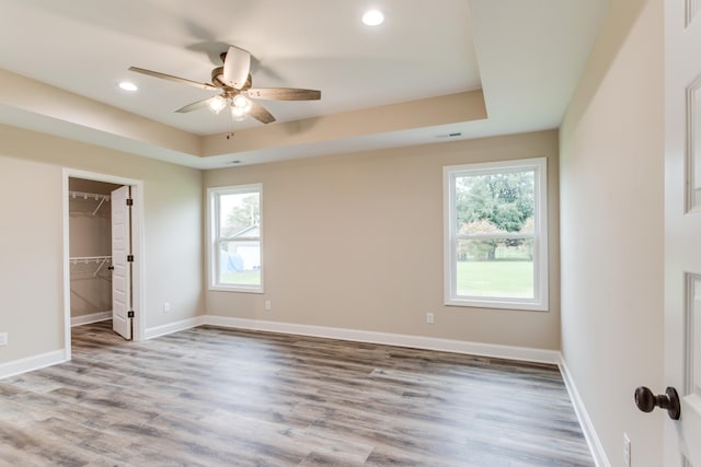 unfurnished bedroom featuring wood-type flooring, a walk in closet, multiple windows, and ceiling fan